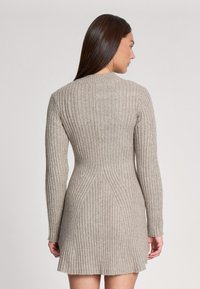 Abito a maglia beige a coste con maniche lunghe, busto aderente e orlo svasato. Le linee verticali creano una silhouette strutturata.