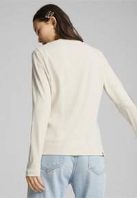 Dlouhý rukáv ribbed top v off-white, s klasickým kulatým výstřihem a zakřiveným lemem. V kombinaci s světle modrými džíny, které zdůrazňují detaily na zadní straně.