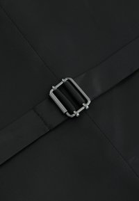 Superficie textil negra que presenta una correa plana asegurada por una hebilla de metal plateado. El material tiene una textura suave con un brillo sutil.