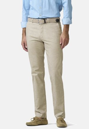 Mann trägt beige karierte Hosen mit einem gewebten beigen Gürtel, ein hellblaues Hemd mit aufgeknöpften Ärmeln und braune Wildlederloafer.