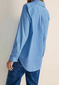 Ljusblå långärmad skjorta med vertikala vita ränder, knäppta manschetter, rygginsats och böjd fåll, tillverkad av ett slätt tyg.