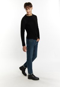 Czarny sweter dzianinowy z prążkowanymi mankietami, w połączeniu z niebieskimi dżinsami. Model nosi czarne sznurowane buty z teksturowaną podeszwą. Prosty, elegancki design.