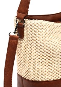 Tan läder- och flätad halm-bucket bag med ett brunt handtag, som har en texturerad yta och kontrasterande material.