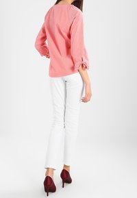 Chemise rayée rouge et blanche à manches trois-quarts, nouée aux poignets, assortie à un pantalon blanc ajusté et des escarpins bordeaux.
