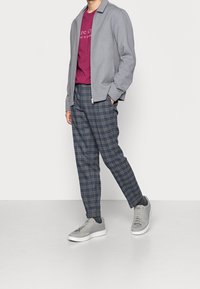 Grå zip-up jakke over en marsala t-shirt, parret med blå ternede bukser og lysegrå sneakers med hvide såler.