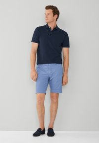 Marineblå polo med korte ærmer, lyseblå shorts og sorte slip-on sko. Afslappet outfit med en løs pasform og enkelt design.
