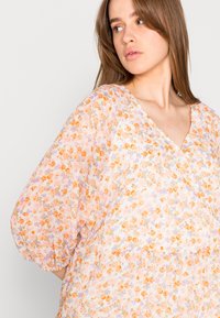 Blusa floral com decote em V, tecido leve e transparente, cores pastéis, mangas bufantes, com padrões de flores laranja e roxas.