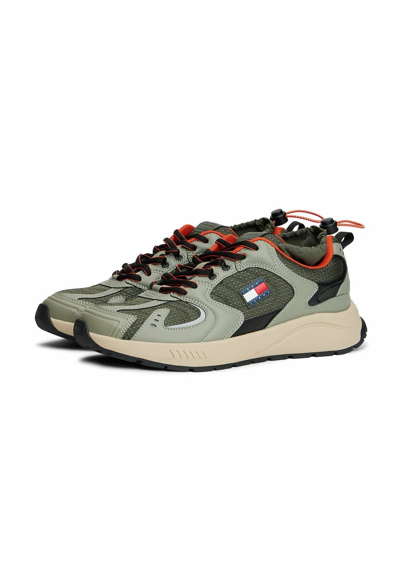 Sporty sneakers featuring a green and black mesh design, red accents, and a textured rubber sole. Includes elastic laces and logo detail.