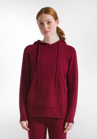 Hanorac cu glugă burgund dintr-un material moale, având un buzunar frontal, șnur de ajustare și mâneci lungi tip raglan; asortat cu pantaloni coordonați.