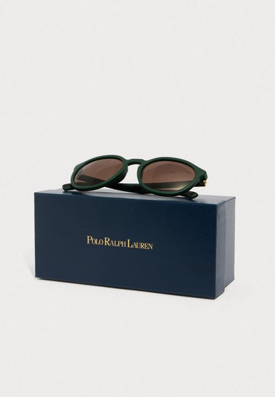 Óculos de sol de plástico verde com lentes ovais e tonalidade castanha, colocados numa caixa azul-marinho com "POLO RALPH LAUREN" em letras douradas.