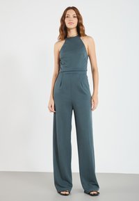 Teal jumpsuit med halterneck, vid ben-design og blød tekstur. Har en tætsiddende bodice og subtile draperinger i taljen.