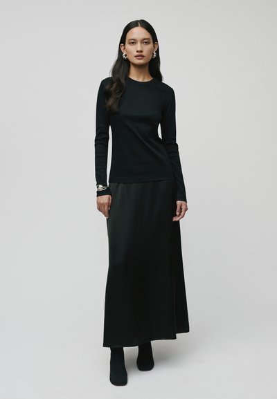Schwarzes Langarmoberteil kombiniert mit einem schwarzen Satin-Maxirock. Das Outfit zeichnet sich durch ein figurbetontes Design und eine glatte Textur aus, das bis zum Knöchel reicht.