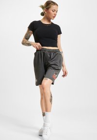 Svart cropped t-skjorte kombinert med grå treningsshorts med en brodert logo. Modellen har på seg hvite sneakers og ankelstrømper.