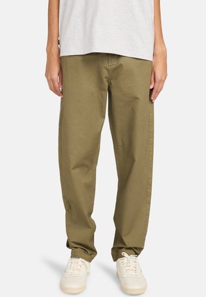 Olivegrüne Baumwollhose mit lässiger Passform, Seiten pockets, glatter Textur und kombiniert mit weißen Sneakers.