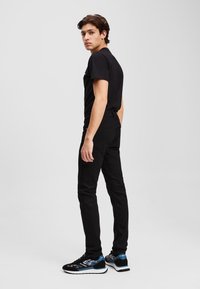 Fekete, rövid ujjú p�óló fekete slim-fit farmernadrággal párosítva. A lábbeli fekete és kék árnyalatok keverékét, valamint mintás dizájnt visel.