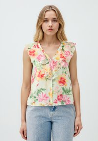 Ärmellose Blumenbluse in Hellgrün, mit einem fransigen V-Ausschnitt, lebhaften rosa und gelben Blumen sowie einer Knopfverschlüsse entlang der Vorderseite.