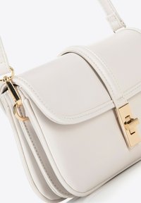 Borsa a mano in pelle crema con chiusura a sottogola, hardware dorato e finitura testurizzata. Presenta una sottile tracolla e un design minimalista.