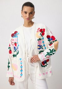 Valge broderdatud kardigan, millel on värvilised lille- ja abstraktsed mustrid. Includes on sidekinnitus ja kaks esist taskut. Puuvillane materjal.