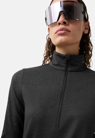 Sort atletisk quarter-zip-overdel med en glitrende tekstur og høj krave, kombineret med oversize spejlreflekterende solbriller.