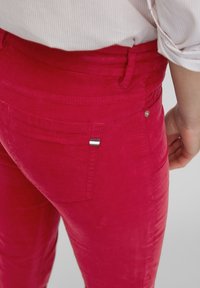 Heldere roze corduroy broeken met een achterzak die een klein gestreept detail en een metalen buttonaccent heeft. Soepele textuur met een getailleerd ontwerp.