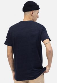 Camiseta de manga corta azul marino con cuello circular. Textura de tela suave. Presenta un pequeño parche con el logo en la manga izquierda.