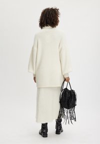 Suéter blanco, esponjoso y de gran tamaño con mangas largas, combinado con una falda a juego. Bolso negro con flecos. Botines negros con hebillas.
