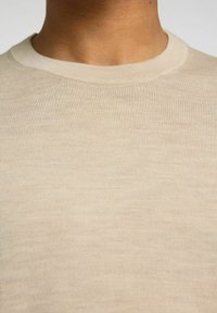 Μπεζ πουλόβερ με λαιμόκοψη, ριγωτή υφή, ελαφρύ ύφασμα, χωρίς ραφές στους ώμους και λεπτές παραλλαγές στο χρώμα σε όλη την ύλη.