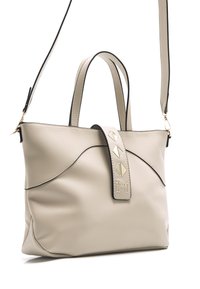 Sac à main en cuir beige avec un design incurvé, bord noir, doubles poignées et une bandoulière ajustable. Présente des accents géométriques décoratifs sur le rabat.