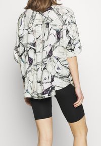 Lättviktsblus med många färger och blommönster, korta ärmar och lös passform, i kombination med svarta cykelshorts.