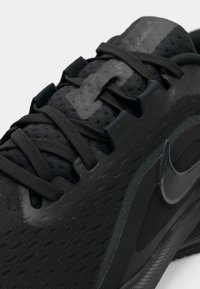 Gros plan d'une chaussure de course Nike noire montrant les lacets, le tissu en mesh et le logo Swoosh brillant sur le côté.