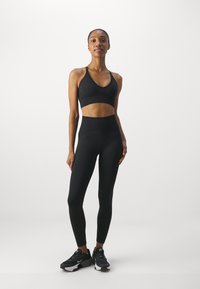 Sutiã desportivo preto e leggings de cintura alta feitos de um tecido liso e elástico, apresentando um design sem costuras e detalhes de costura mínimos.