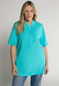 Tyrkysové polo tričko s krátkými rukávy, límečkem a zapínáním na knoflíky. Hladká látka s uvolněným střihem, kombinované s modrými džíny.