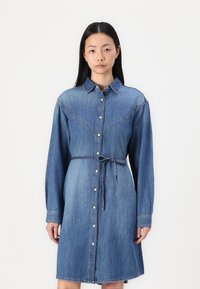 Denim srajčna obleka z dolgimi rokavi, gumbom spredaj, zožanim pasom in rahlo razširjenim robom. Modra denim tekstura s kontrastnimi šivi.
