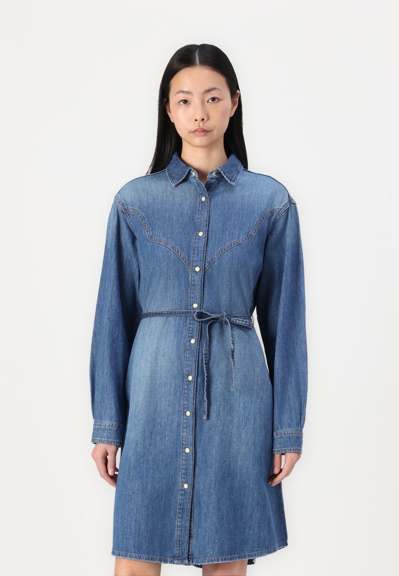 Denim srajčna obleka z dolgimi rokavi, gumbom spredaj, zožanim pasom in rahlo razširjenim robom. Modra denim tekstura s kontrastnimi šivi.