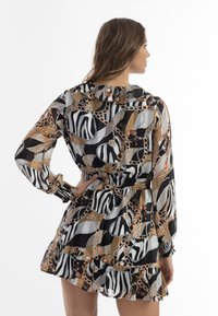 Durchsichtiges, schwarzes Kleid mit einem lebendigen, abstrakten Druck, der zebraähnliche Streifen und Kettenmuster zeigt. Elastischer Taillenbund und rüschensaum. Lange Ärmel.