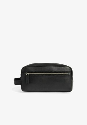 Trousse de toilette en cuir noir avec une poche zippée horizontale à l’avant et une poignée latérale sur fond blanc.