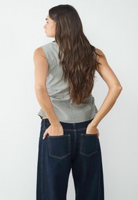 Pasiasty bezrękawnik w jasnoszarym i białym kolorze, połączony z ciemnoniebieskimi szerokimi spodniami dżinsowymi z dwoma tylnymi kieszeniami i widocznym szwem.