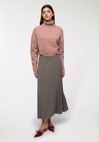 Jasnoróżowy krótki sweter z wysokim kołnierzem, zestawiony z szarym plisowanym spódnicą midi. Modelka ma na sobie czerwone buty na obcasie z kokardkami z przodu.