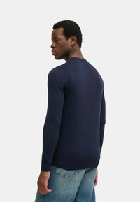 Maglione lavorato a maglia blu navy con maniche lunghe, collo rotondo e dettagli a coste sulle spalle, abbinato a jeans in denim chiaro.