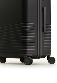 Zwarte harde koffer met gestructureerde lijnen, een zijhandvat en vier draaibare wielen voor gemakkelijke mobiliteit. Duurzaam materiaal en een slank ontwerp.
