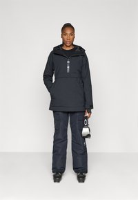 Must have mustad parka, millel on esikott ja tõmblukk, koos sobivate cargo-pükstega. Pükstel on küljetaskud.