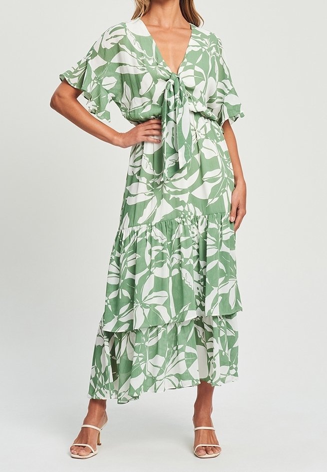 Vestido verde y blanco con estampado floral, escote en V, lazo delantero y falda con volantes en capas. Mangas cortas y acampanadas de tela ligera.