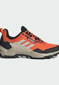 Terrex-sneakers med en lys orange textilöverdel, svarta accenter, reflekterande silverränder och en robust svart sula med mönster.