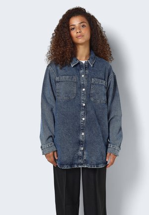 Camicia in denim blu scuro, con fronte a bottoni, due tasche sul petto e maniche lunghe con polsini. Texture invecchiata evidente.