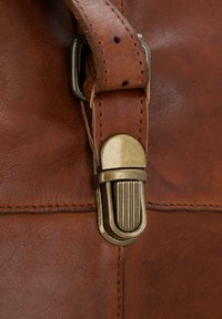 Borsa in pelle marrone con una chiusura metallica dalla superficie testurizzata e una tracolla in pelle coordinata, enfatizzata da dettagli di cucitura visibili.