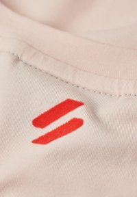 Tessuto rosa chiaro con una texture morbida presenta linee rosse ricamate. La vista ravvicinata evidenzia i dettagli della cucitura e la qualità del tessuto.