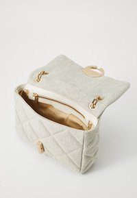 Quiltet lys beige håndtaske med guldfarvede detaljer, der har en klaplukning, en lynlås lomme indeni og en glat inderforing.