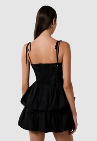 Robe noire avec un corsage fitted présentant des détails plissés et des bretelles réglables, se déversant en une jupe évasée à étages. Texture lisse.