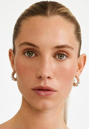 Silver hoop earrings with a circular design, smooth texture, and polished finish, worn by a person with a neutral background.