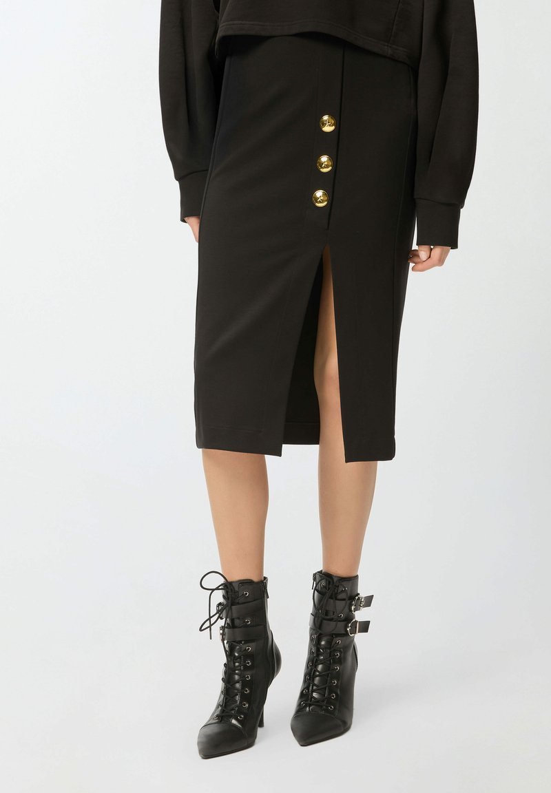 Gonna midi nera con spacco frontale e quattro bottoni dorati. Abbinata a stivali con tacco neri con lacci, fibbie e punte appuntite.